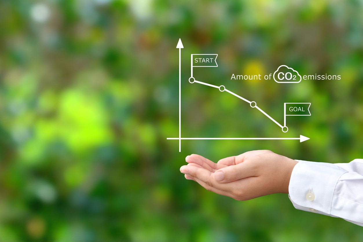 Child's hands covering downward CO2 emissions graph on natural green background